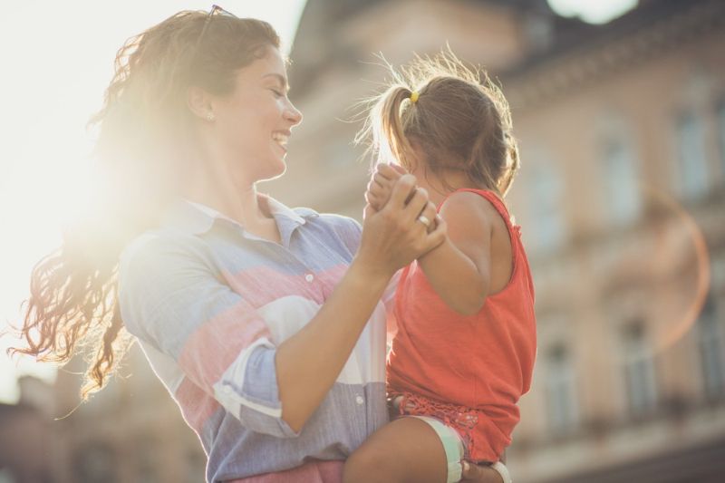 single mother smiling and holding her daughter during sunset
