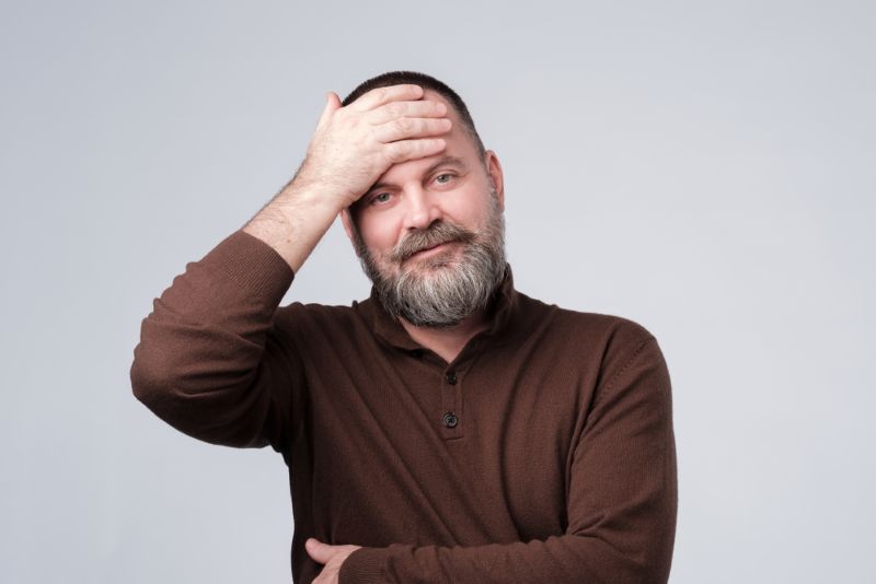 older man standing with hand on head