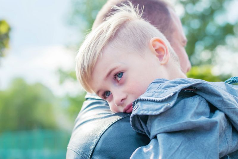 Closeup image of a sad young boy being held by his father