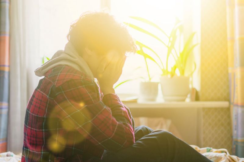 Disgruntled teen sitting in bed with hands over his face