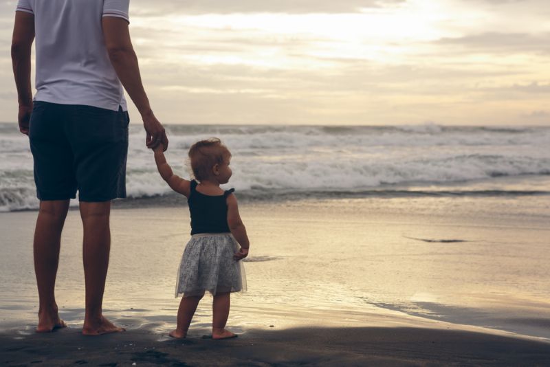 Single father holding his daughter's hand on the beach